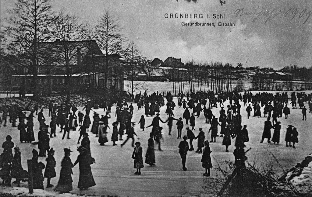 Czarnobiała pocztówka z Zielonej Góry (Grunbergu). Przedstawia ludzi na lodowisku. W tle widać dom.